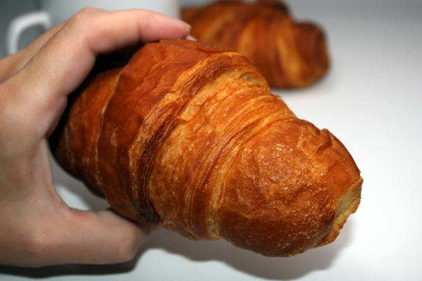 istock Fresh crispy croissant close-up in hand. Blurred light background. Cooking, home baking. 1414284031