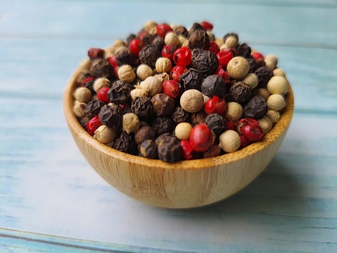 Peppercorns: black, white and pink, in a wooden bowl, isolated on a wooden table, selective focus with space for text.