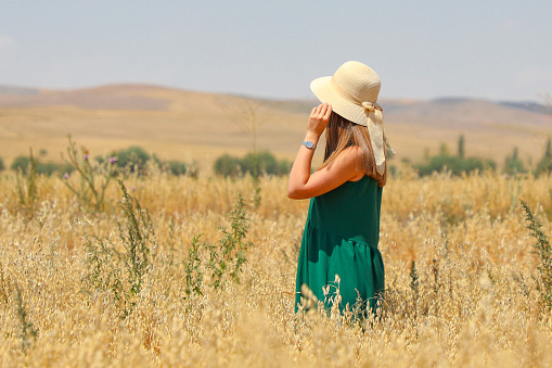 A blond-haired woman in a hat in a field of oats