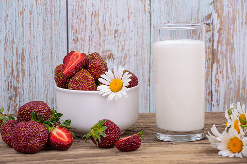 A glass of fresh milk and a plate of ripe red strawberries on a wooden background, close-up