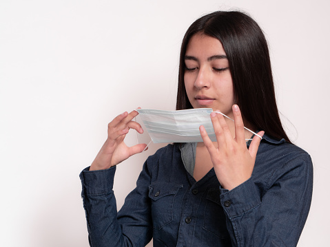 portrait of black-haired latina girl putting on surgical mask, isolated on white background