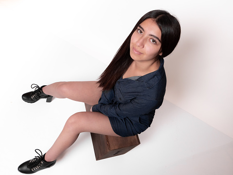 latina girl with black hair and short skirt sitting on apple box isolated on white background