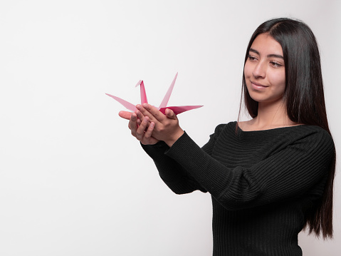 cute smiling latina girl dressed in black outfit, showing a crane, side view of girl, isolated on white background, otaku concept.