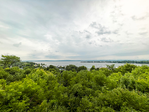 Scenic Views on a Bluff Overlooking Lake Michigan. Tall green, leafy trees in the foreground. A beautiful bay of water and peninsula  can be seen in the distance. Dramatic cloudscape overhead. Located in Harbor Springs, Michigan, USA.