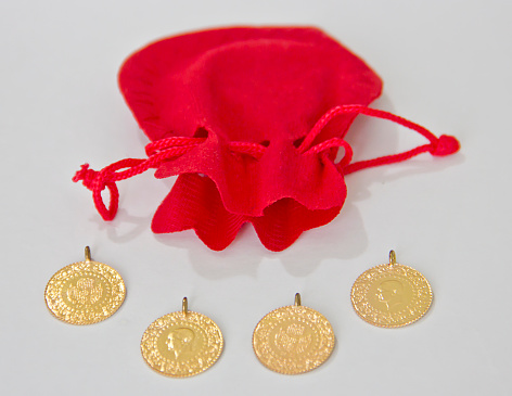 Pours the Turkish gold coins into the red pouch. Gold coins in grey bag on wooden background. Finance concept. English mean of text on coins is