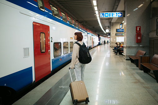 Young adult woman waiting for her train on a subway station and holding her luggage next to her