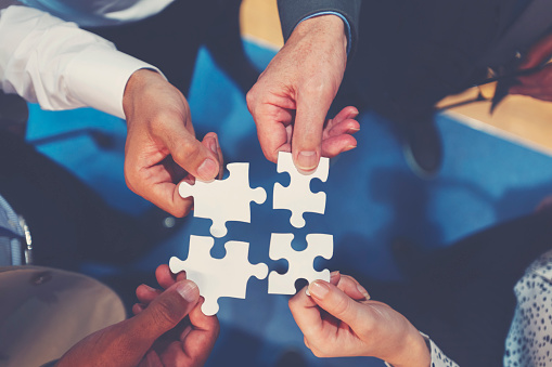 Group of business people holding a jigsaw puzzle pieces. Business solution integration concept. Multi ethnic group. Close up of hands high angle view directly above