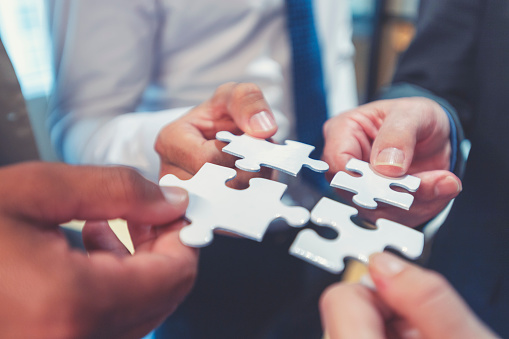 Group of business people holding a jigsaw puzzle pieces. Business solution integration concept. Multi ethnic group. Close up of hands