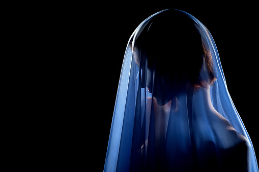 woman under blue veil posing sensually on black background with copy space, profile side view