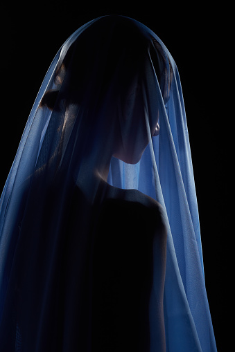 sad woman under blue veil posing on black background, rear back view