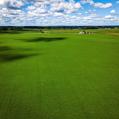 A cloudy blue sky extends to the horizon with a massive farm field below surrounded by a rural area in Wisconsin.