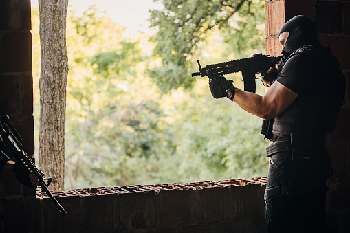 SWAT team soldier standing on his position by the window with gun on a mission in abandoned building.
