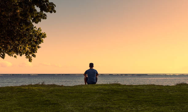 istock Man sitting on the beach at sunset. 1414307296