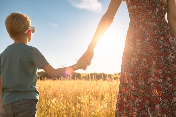 istock Mother and son holding hands in field at sunset 1414308024