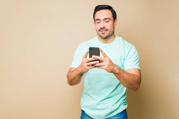 istock Attractive man sending online text messages on his phone and smiling 1414308099