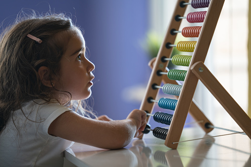 Close up photo of preschooler girl using wooden abacus. The abacus is multicolored. Shot indoor with a full frame mirrorless camera.