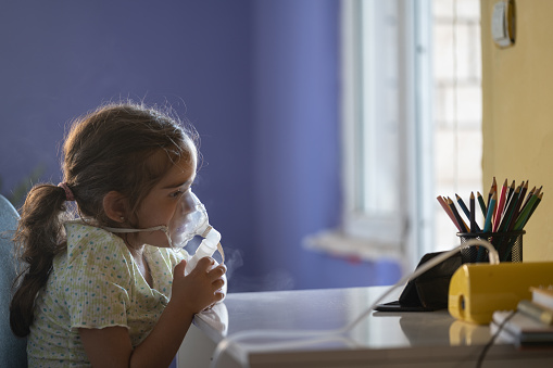 Close up photo of 3 years old girl sitting in living room and using nebulizer for allergy treatment. Shot indoor with a full frame mirrorless camera.