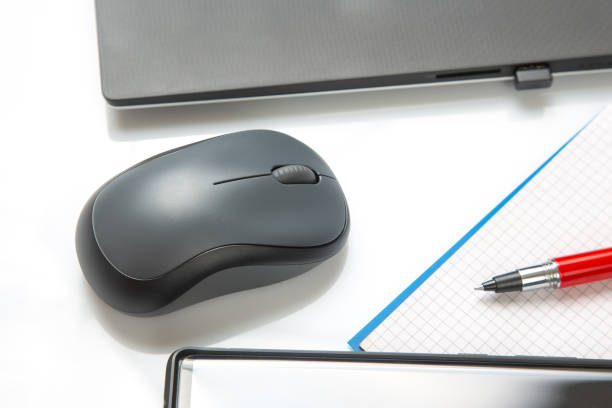 istock Computer wireless mouse, pen and notepad next to a laptop on a white table close-up. Items for office work 1414313534