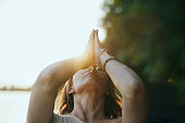A yogi woman holds her hands in a namaste position and prays while exercising yoga on the dock near the river in nature.