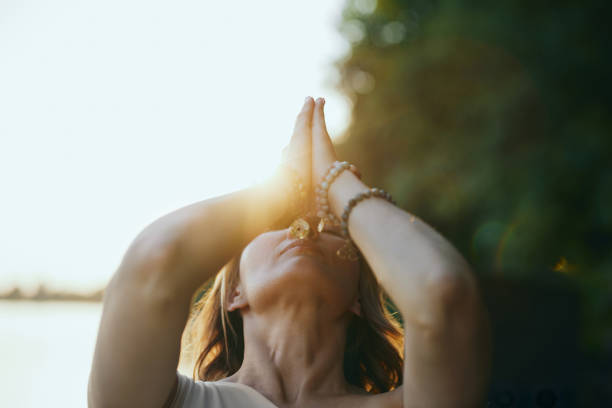 A yogi woman holds her hands in a namaste position and prays while exercising yoga on the dock near the river in nature. stock photo