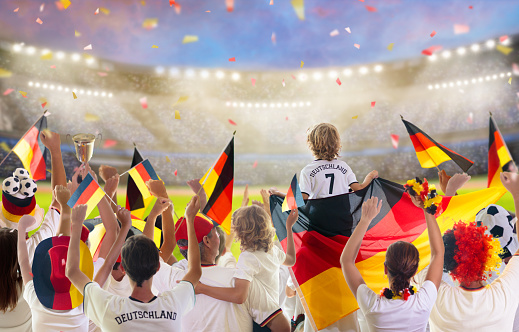 Germany football supporter on stadium. German fans on soccer pitch watching team play. Group of supporters with flag and national jersey cheering for Germany. Championship game.