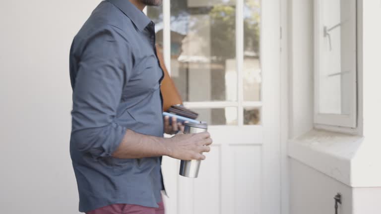 Man leaving his house with his everyday items and a travel mug