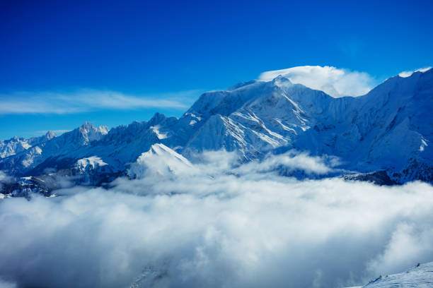 Flying above clouds: view of mountains with high Alps peaks of Mont Blanc massif on background on sunny day