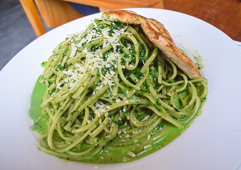 Spaghetti Pesto peruvian way with grilled  chicken breast, served in a white dish, on a table in a peruvian restaurant.