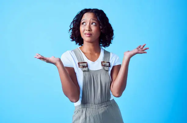 Photo of Confused, puzzled and clueless woman with pensive facial expression and looking up in doubt throwing her hands aside. Portrait of beautiful, edgy and unsure Asian female isolated over blue background