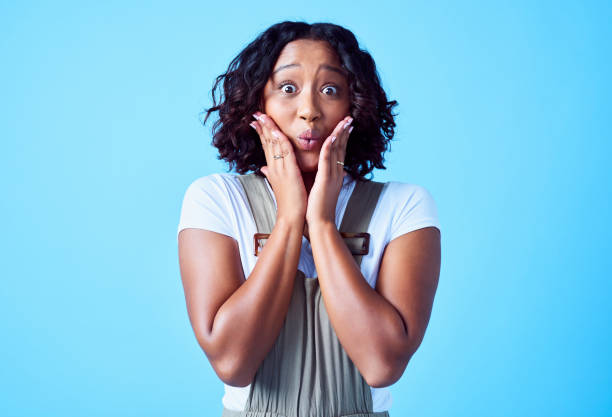 istock Shocked, surprised and excited young female holding her face with her hands while feeling cheerful. Portrait of a shocked woman in surprise. Casual lady with big eyes looking joyful and amazed. 1414324436