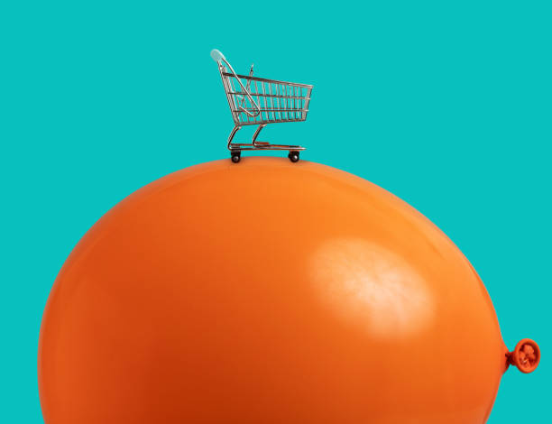 Inflation and shrinking purchasing power concept: shrinking shopping cart on huge orange balloon stock photo