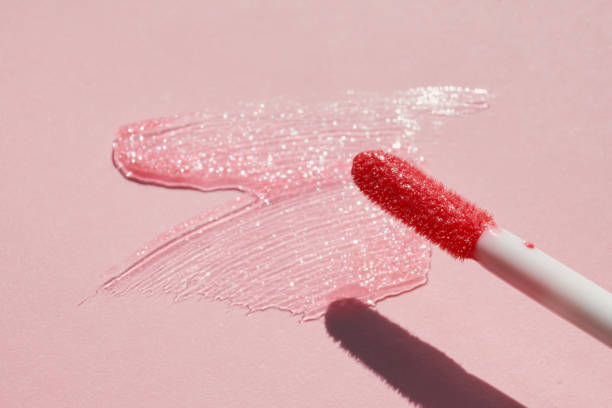 Smears of shining lip gloss and lip gloss brush on pink background, hard shadows Smears of shining lip gloss and lip gloss brush on pink background, hard shadows. lipstick smudged lip balm shiny stock pictures, royalty-free photos & images