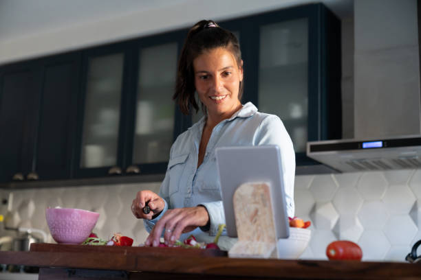 istock Cheerful woman at home following an online tutorial of a vegan recipe using a tablet while chopping vegetables 1414336451