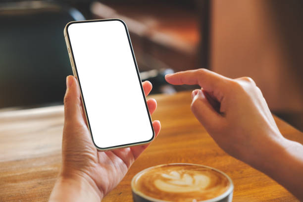 istock Mockup image of hands holding and touching on mobile phone with blank desktop screen with coffee cup on wooden table 1414336706