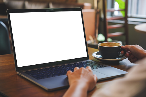 Mockup image of a woman using and working on laptop with blank white desktop screen while drinking coffee