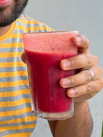 Stock photo showing close-up view of unrecognised man drinking strawberry fruit juice smoothie, as part of five a day fruit and vegetable portions. Healthy eating concept.