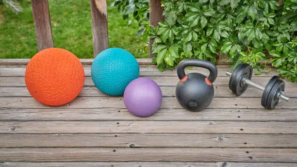 three heavy slam balls, iron kettlebell and dumbbell on a backyard deck, home and backyard gym concept