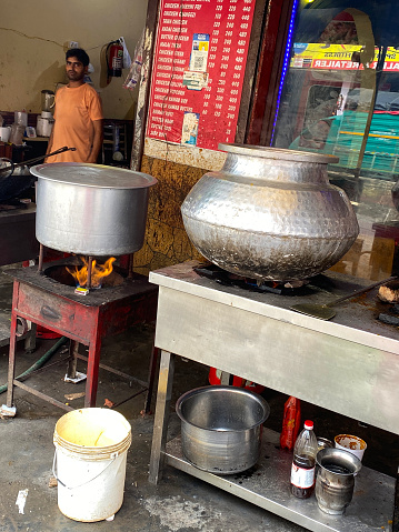 Ghaziabad, Uttar Pradesh, India - July 21, 2022: Stock photo showing Indian street food vendor in local market in a small outdoor stall making and cooking a mixed rice dish of chicken biryani in a large round pan. The pan is on the gas stove on high heat.