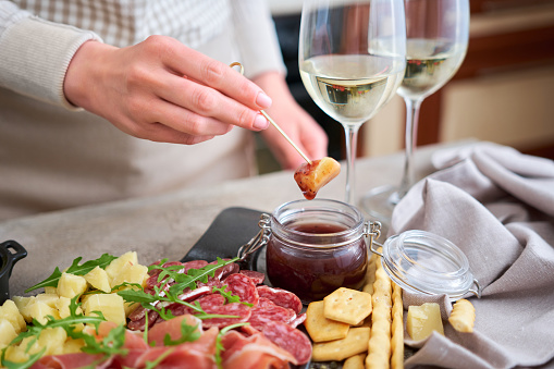 woman dips parmesan cheese into sauce, Two glasses of white wine and Italian antipasto meat platter.