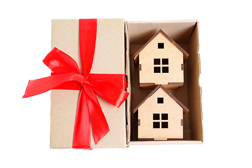 Two wooden toy houses inside a small shipping box with a red ribbon bow. Creative real estate deal concept.