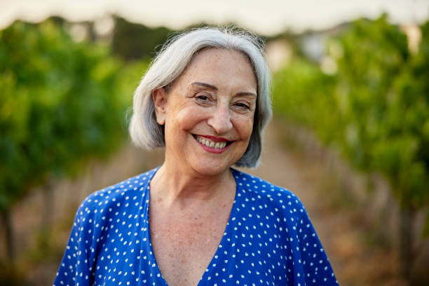 Cheerful senior woman standing between grapevines