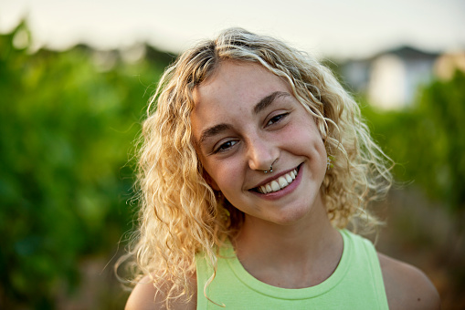 Close view of wine lover with curly blond hair wearing chartreuse tank top and smiling at camera with head cocked.