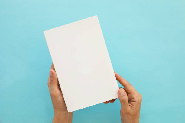 istock Cropped Hands of Man Holding Blank Book Against Blue Background 1414364731