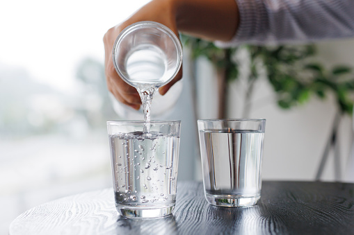 Close up hands of active strong man pouring clean water into glass. Attractive thirsty male drink or take a sip of mineral natural in cup after wake up for health and wellbeing in kitchen in house.