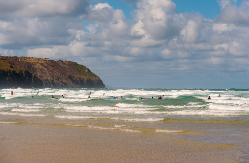 The sun shines down on surfers and bodyboarders playing in the surf at Perranporth Beach in Cornwall.