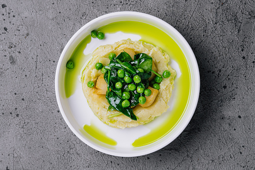 Mashed potato with butter, green peas, basil in a white bowl