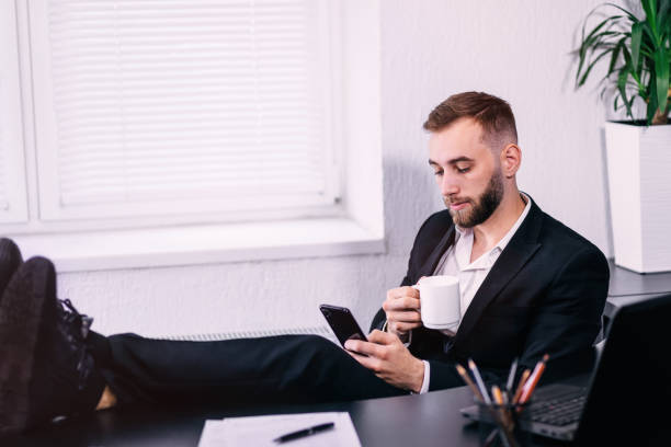 un homme en chemise blanche et costume noir posa ses pieds sur le bureau - desk on the phone sitting table photos et images de collection