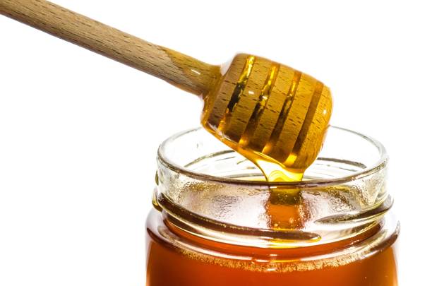 Honey in a glass jar with wooden honey dipper stock photo