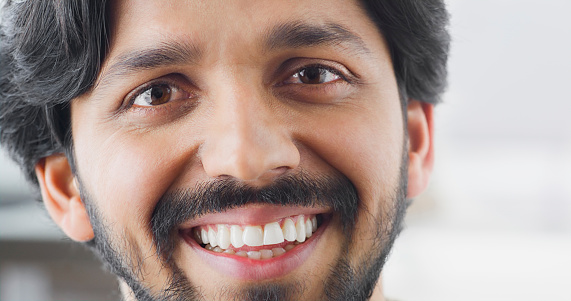 Close-up of smiling young man with brown eyes and beard looking into camera.