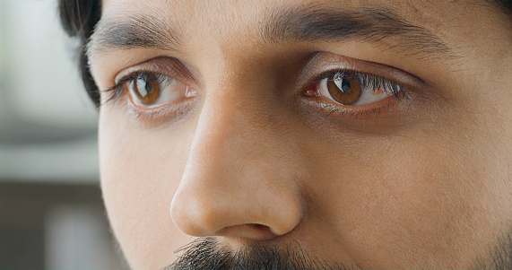 Close-up of thoughtful young man with brown eyes looking away.